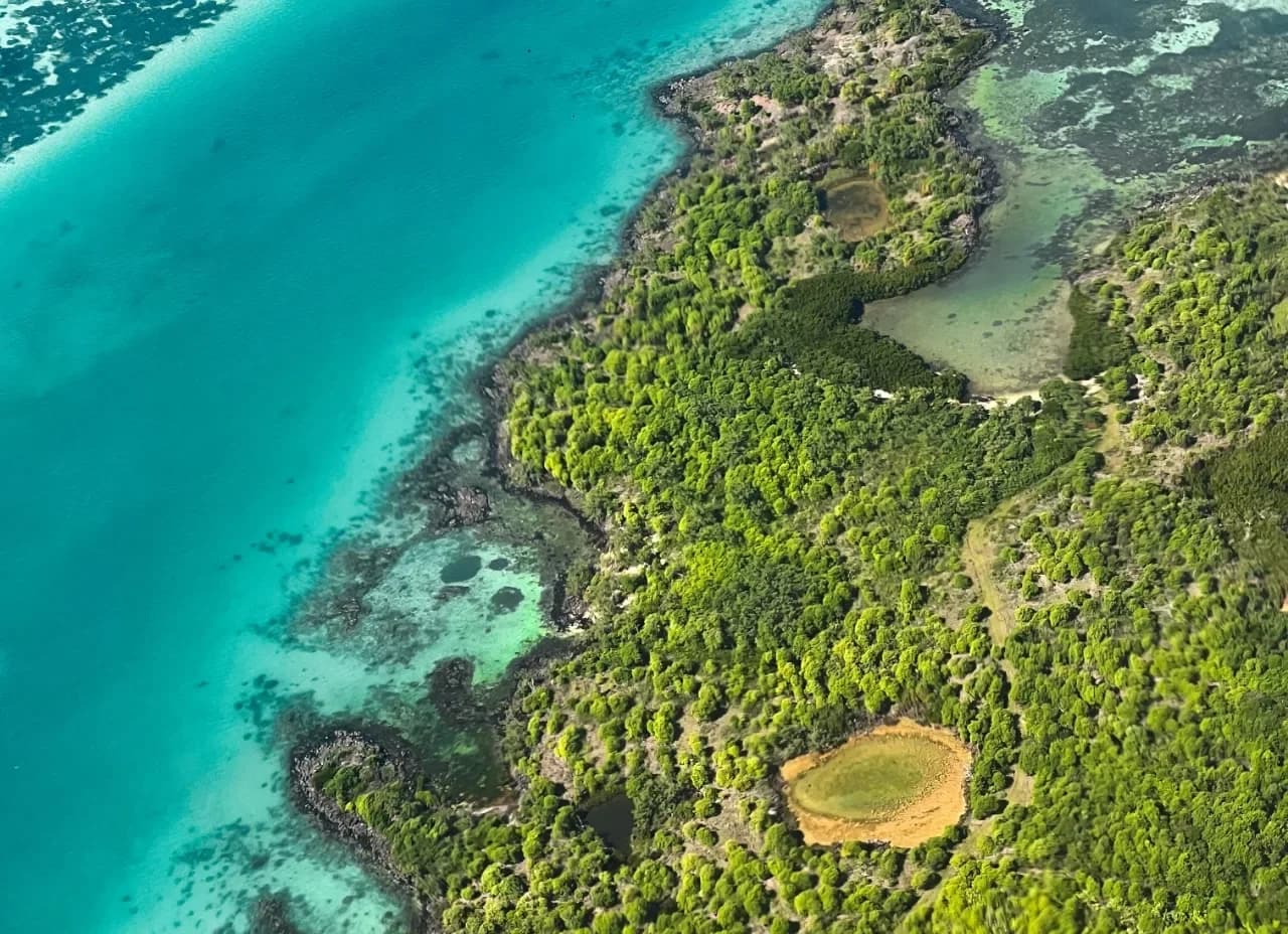 Luftaufnahme einer Sandbank und eines Riffs, an dessen Außenkante sich die Wellen brechen