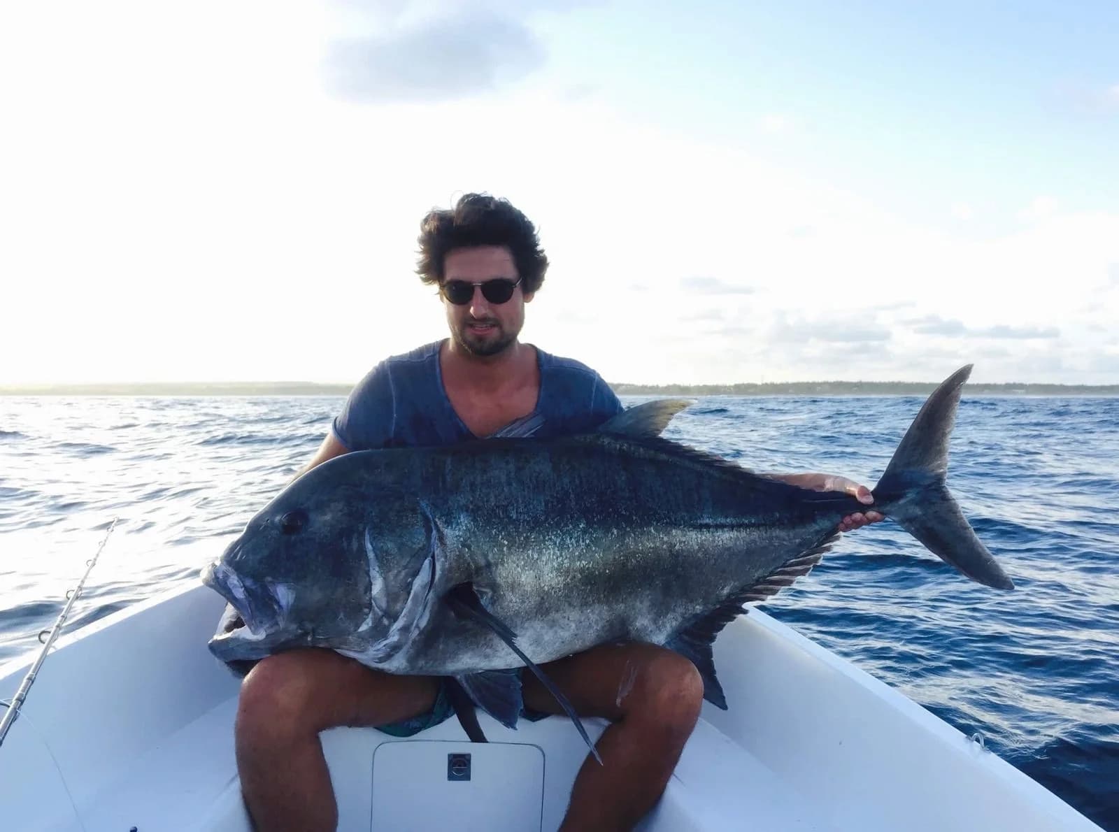 An angler on the bow of the boat holding a very large giant trevally