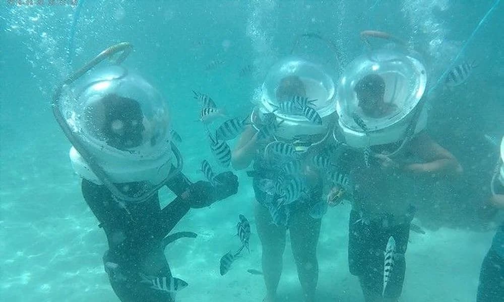 Three guests wearing undersea-walk helmets on the seabed at Belle Mare