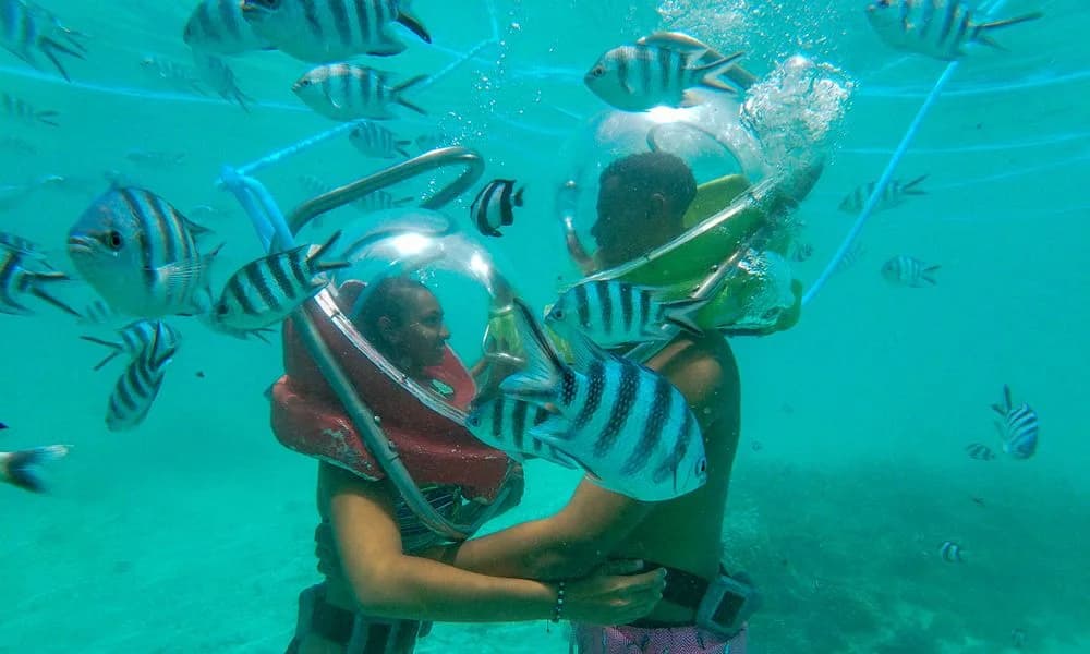 Two Aquacity guests wearing undersea-walk helmets among striped fish in Belle Mare Lagoon