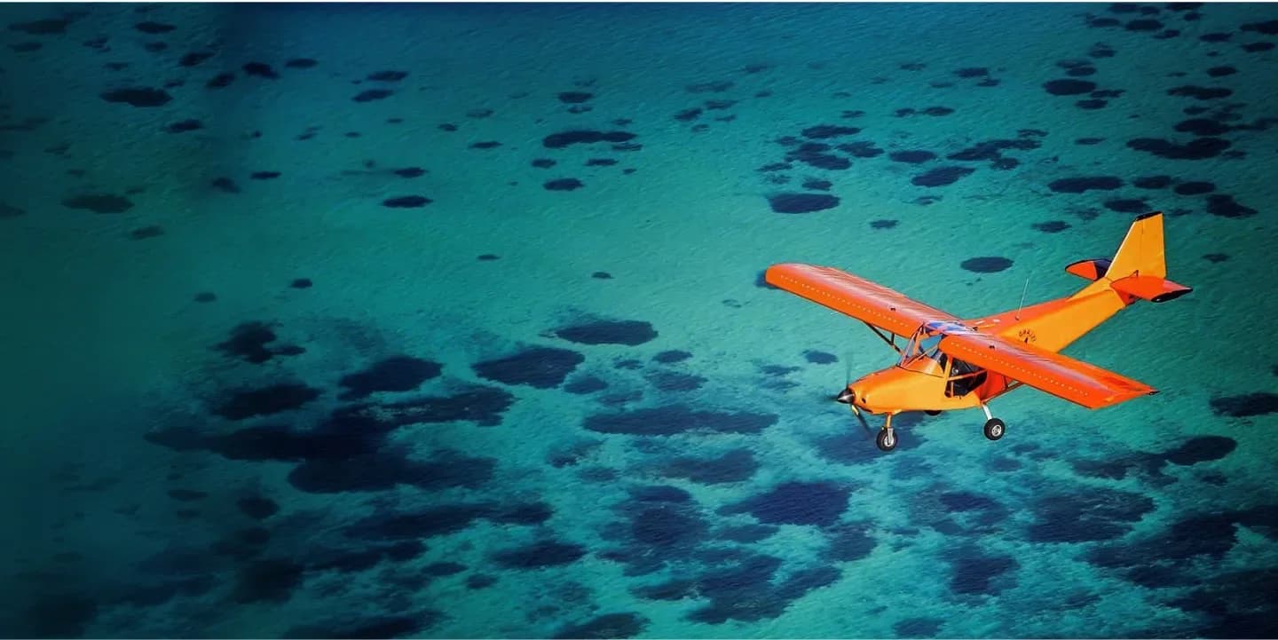 Un ultraleggero arancione in volo sopra le formazioni coralline della laguna