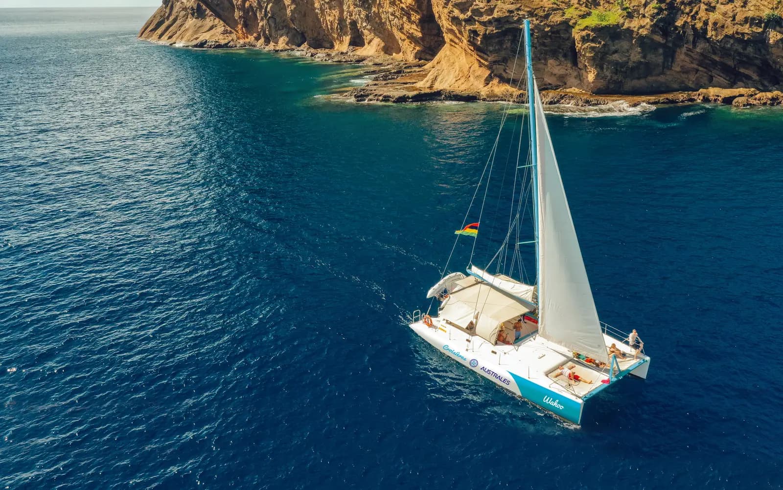 A catamaran sailing beside a rocky island coastline