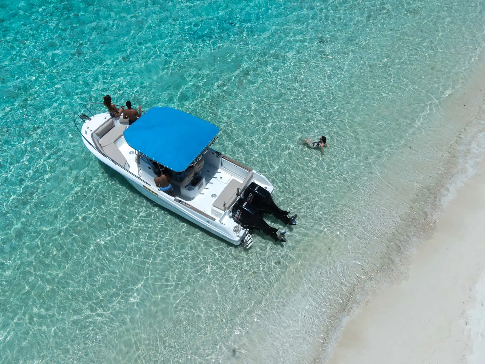 Un bateau à moteur ombragé et un nageur près d’une plage de sable blanc