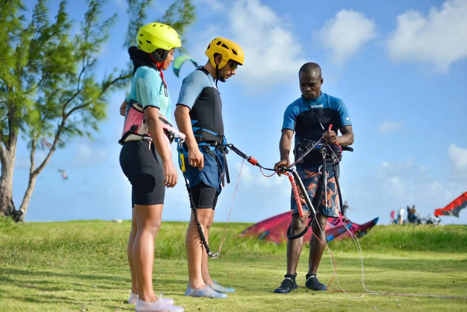 An instructor demonstrates kite lines to two helmeted participants at Le Morne.